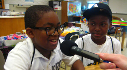 A youth looking at another youth speaking into a held microphone in a classroom