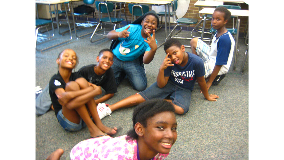 Six youth sitting on the floor smiling and posing for the camera in a classroom