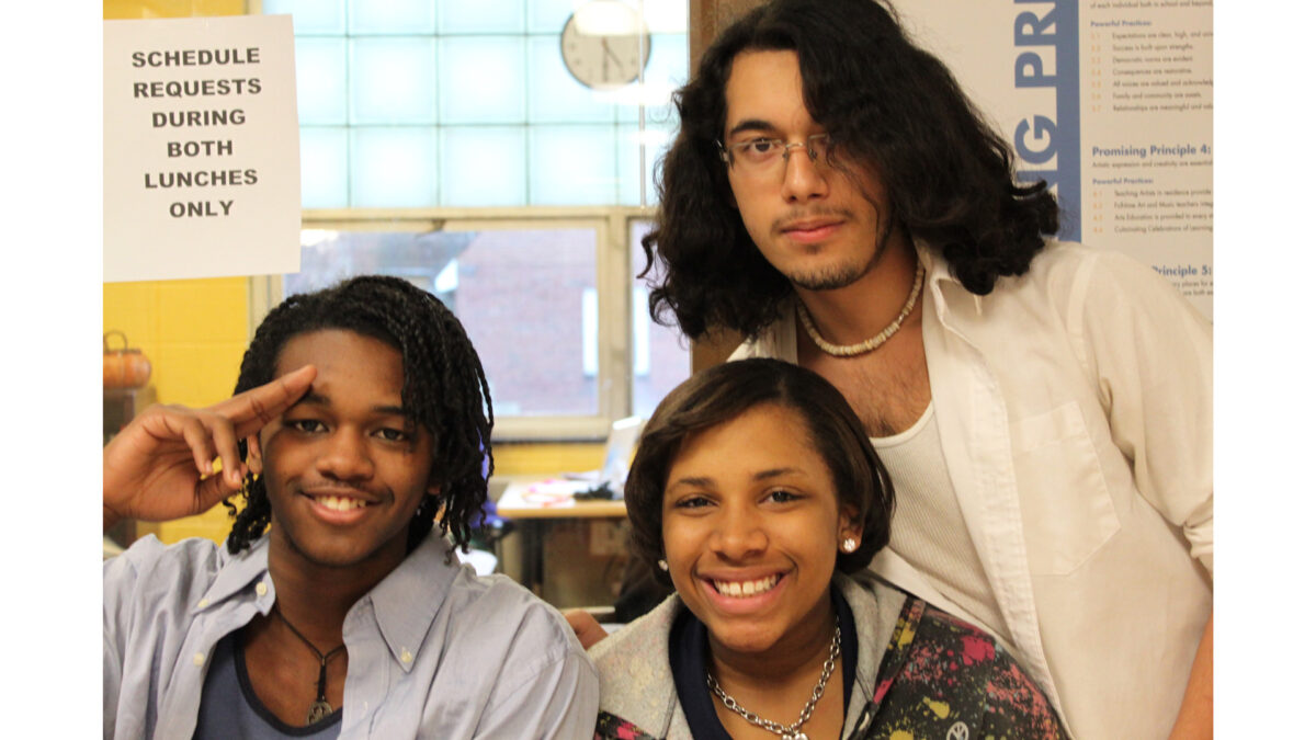 Three teens smiling and posing in a classroom