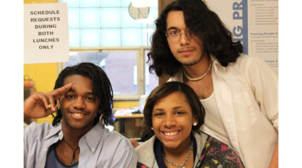 Three teens smiling and posing in a classroom