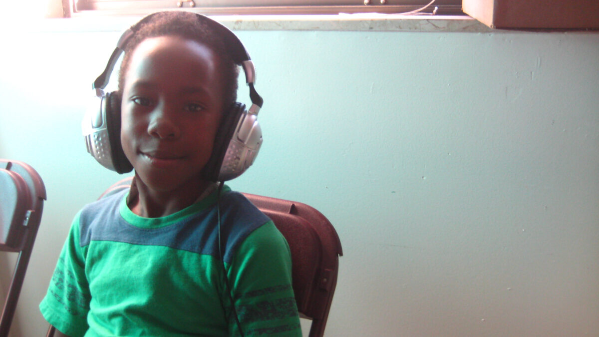 A youth wearing headphones sitting and smiling at the camera