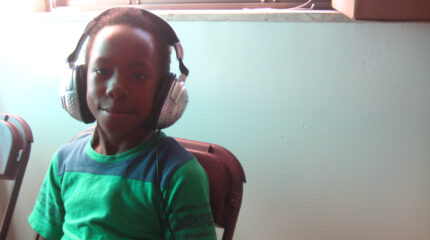 A youth wearing headphones sitting and smiling at the camera