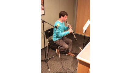 A teen playing oboe looking at sheet music on a music stand in a radio studio