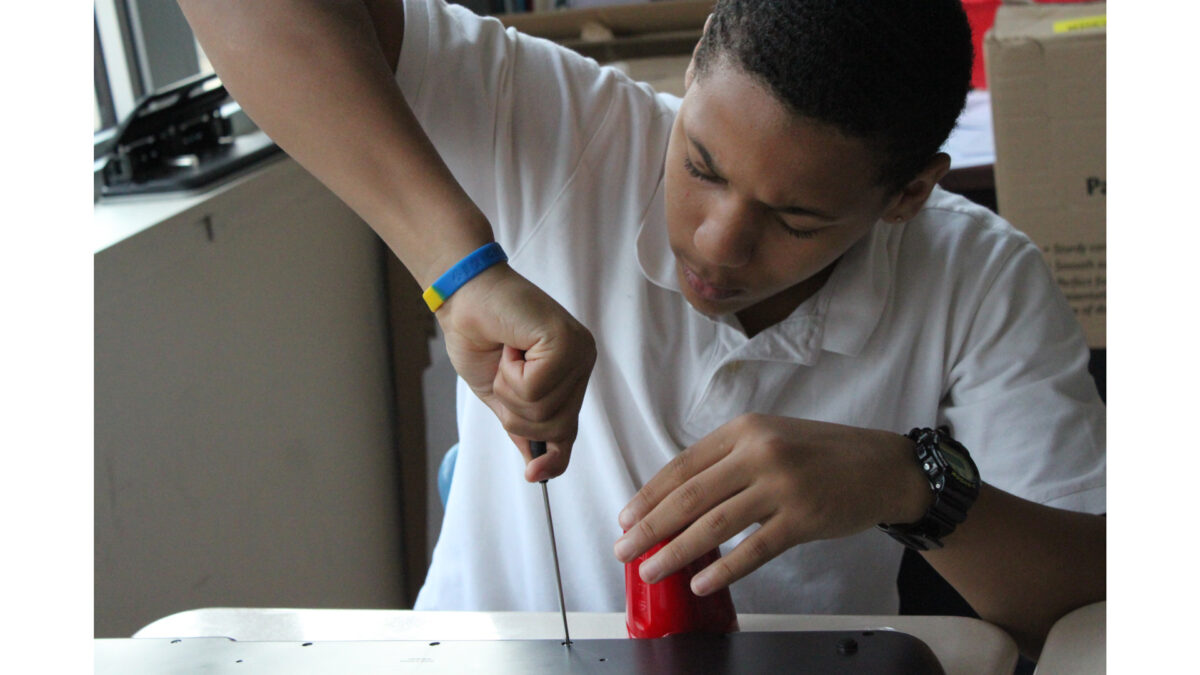A teen screwing a screw with a screwdriver into a panel on a classroom desk