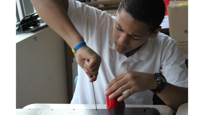 A teen screwing a screw with a screwdriver into a panel on a classroom desk