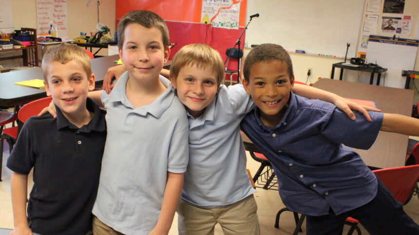 Four youth smiling and posing with their arms around their shoulders in a classroom