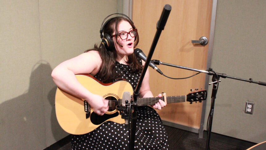 A teen playing an acoustic guitar and singing into a microphone in a radio studio