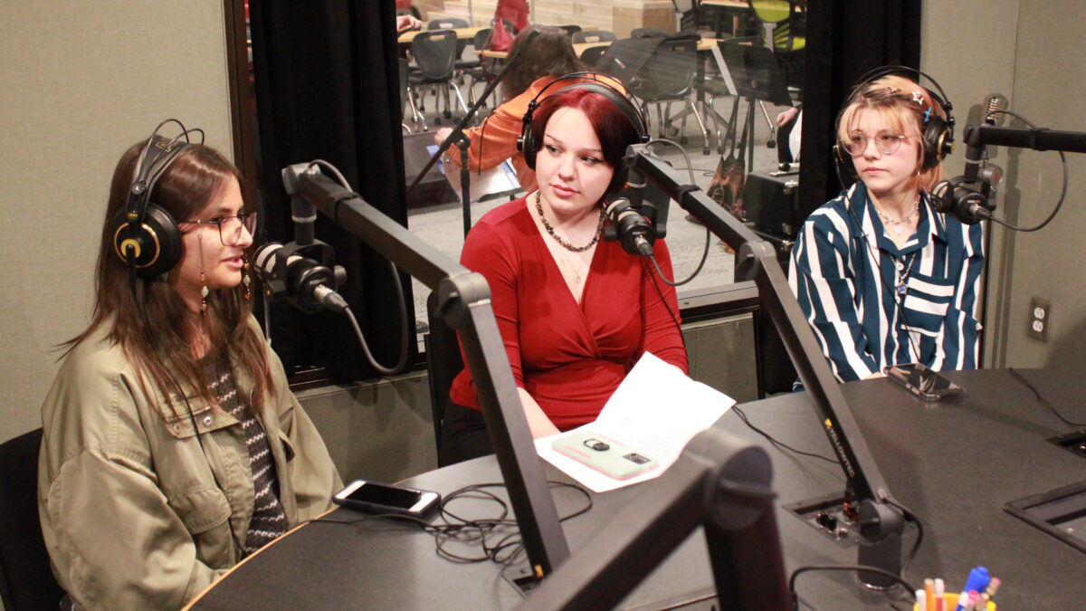 Three teens wearing headphones speaking into microphones in a radio studio