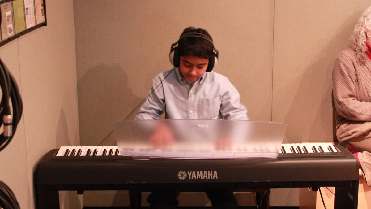 A youth wearing headphones playing a piano keyboard in a radio studio