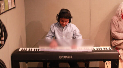 A youth wearing headphones playing a piano keyboard in a radio studio