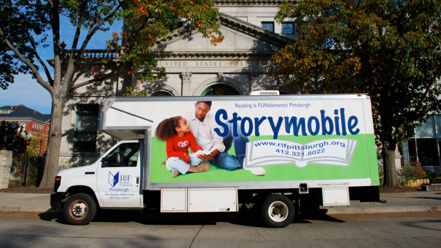 A large box truck with the text "Storymobile" running along the side parked in front of a large marble building with the text "United States Post Office" on the front
