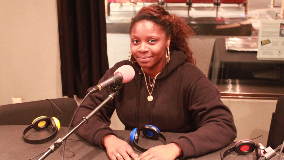 A teen smiling while sitting behind a microphone in a radio studio