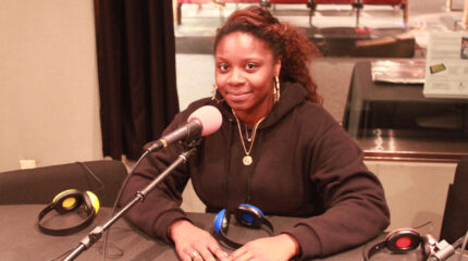 A teen smiling while sitting behind a microphone in a radio studio