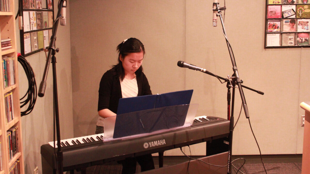A teen playing a piano keyboard looking at sheet music in a radio studio