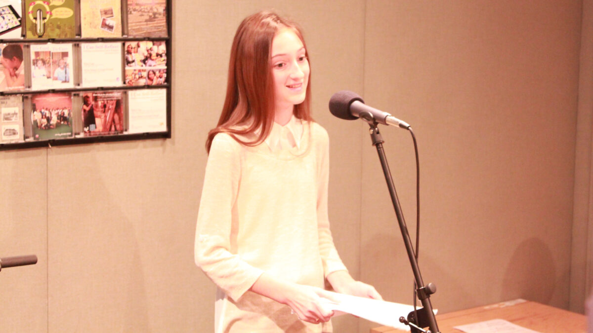 A youth holding a piece of paper and standing behind a microphone in a radio studio