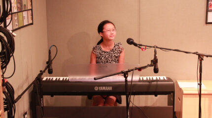 A youth sitting behind a piano keyboard and a microphone in a radio studio