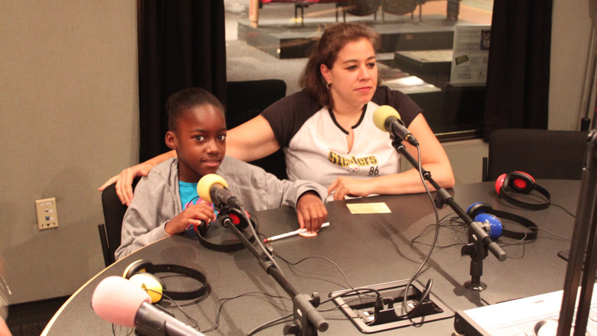 A youth and an adult sitting behind microphones and headphones in a radio studio