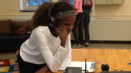 A youth wearing headphones looking at a laptop computer in a classroom