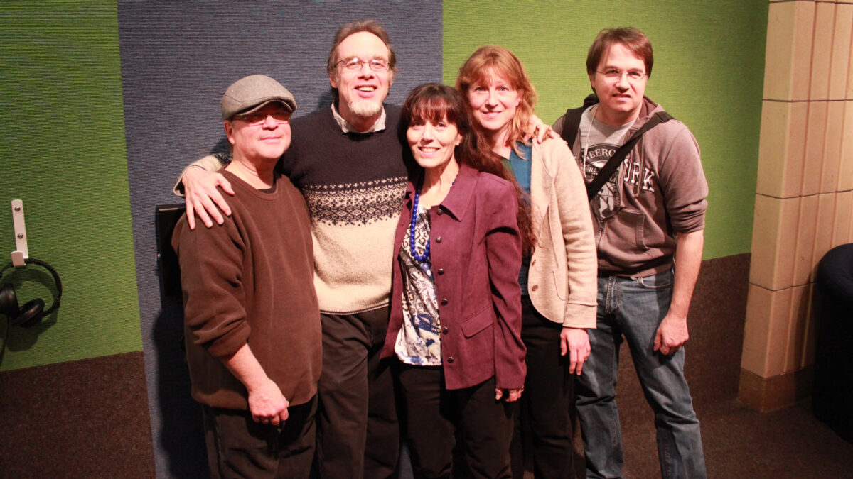 Five adults smiling and standing in profile in front of a green and blue carpet wall