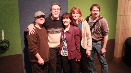 Five adults smiling and standing in profile in front of a green and blue carpet wall