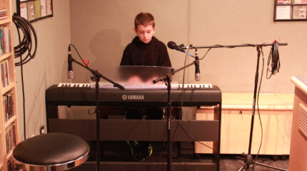 A youth playing a piano keyboard sitting behind microphones in a radio studio