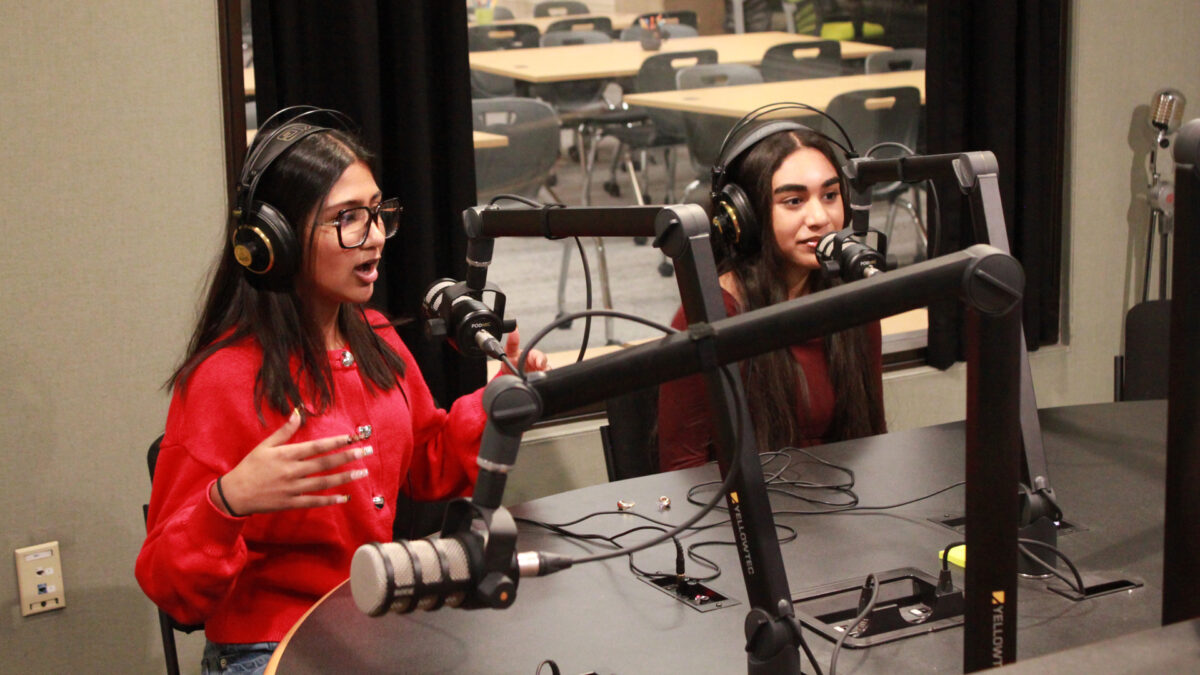 Two teens wearing headphones speaking into microphones in a radio studio