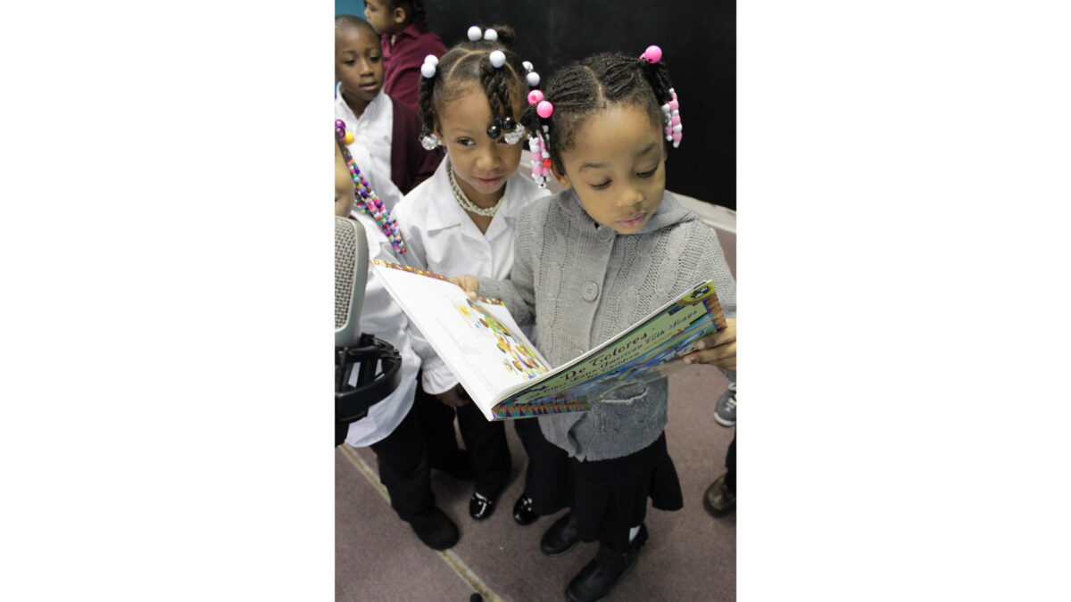 Three youth looking at a book while standing behind a microphone