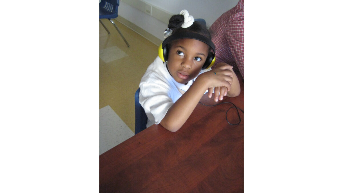 A youth wearing headphones looking up and to the left while leaning their elbows on a brown table