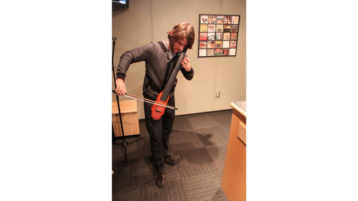 An adult playing an oddly shaped cello in a radio studio