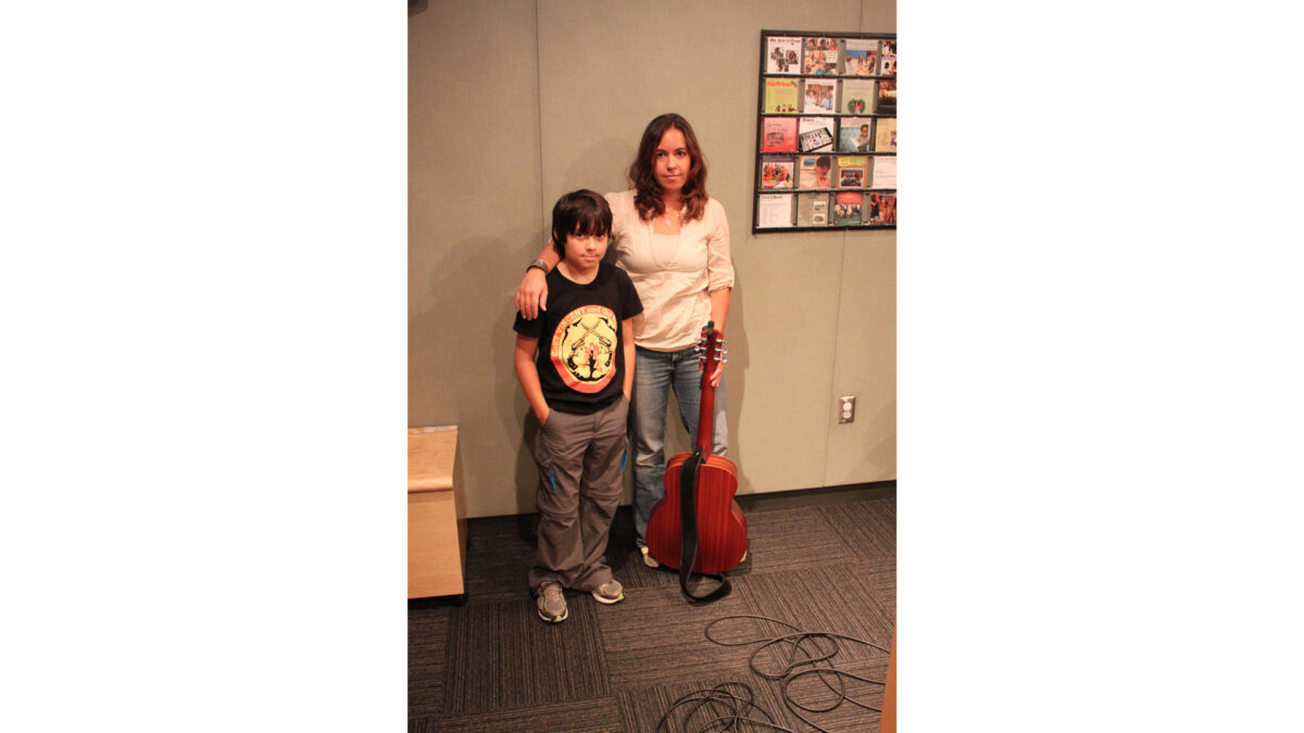 An adult holding a guitar and a youth posing in profile in a radio studio