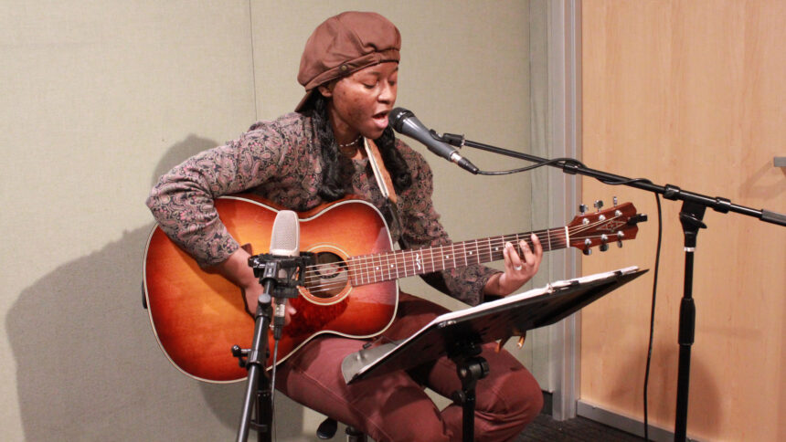 An adult playing acoustic guitar and singing into a microphone in a radio studio