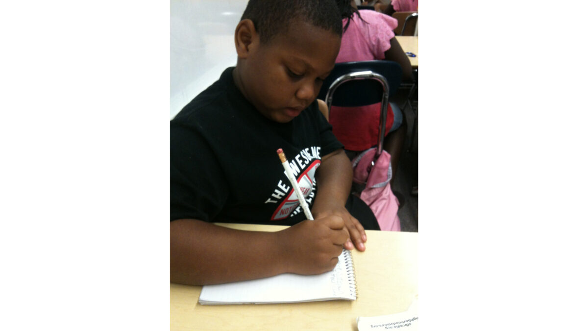 A youth writing on a notebook sitting at a classroom desk