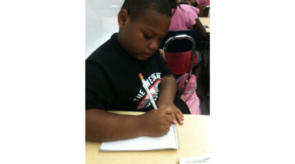 A youth writing on a notebook sitting at a classroom desk