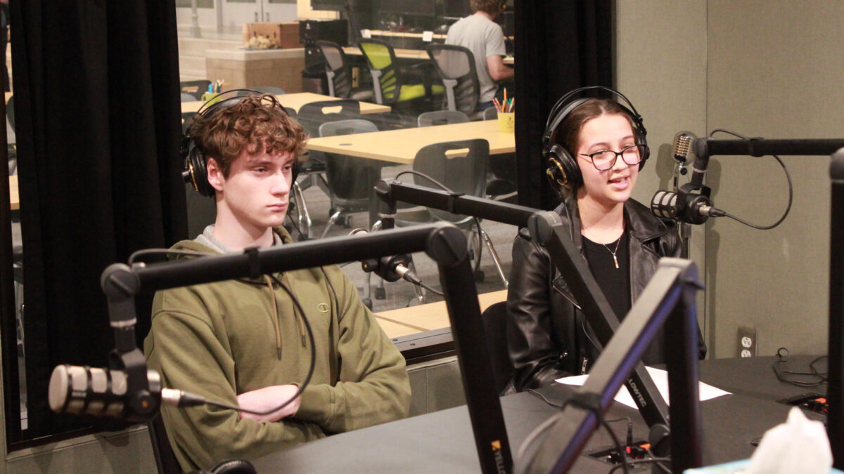 Two teens wearing headphones speaking into microphones in a radio studio