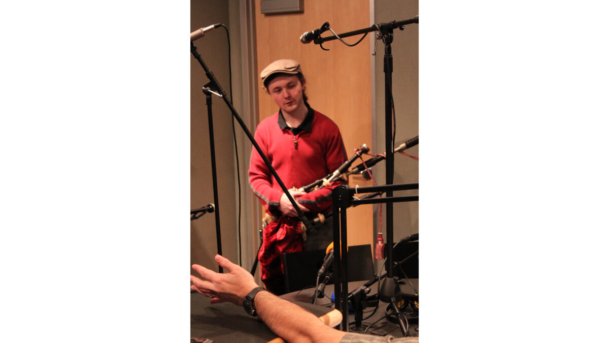 An adult holding a set of bagpipes in a radio studio