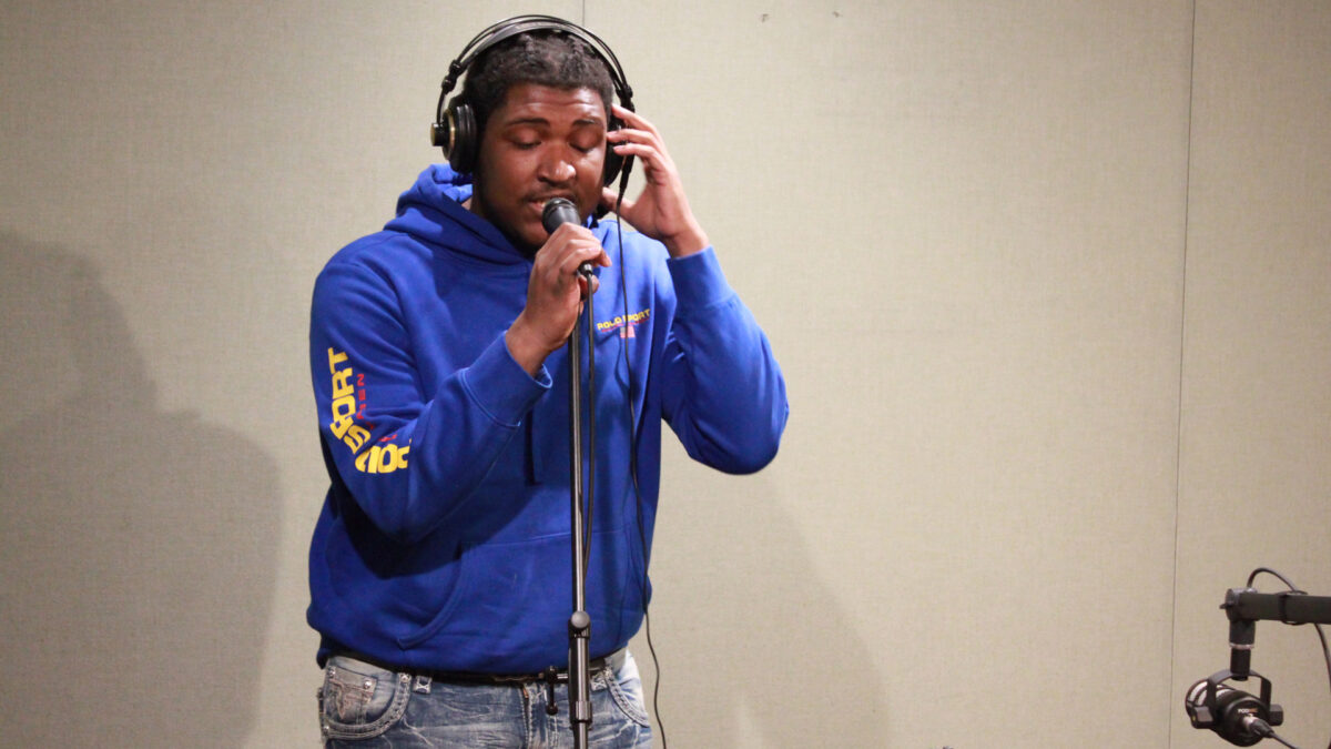 A teen wearing headphones singing into a microphone in a radio studio