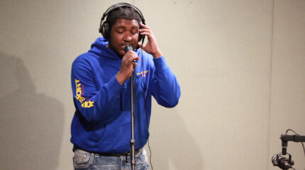 A teen wearing headphones singing into a microphone in a radio studio