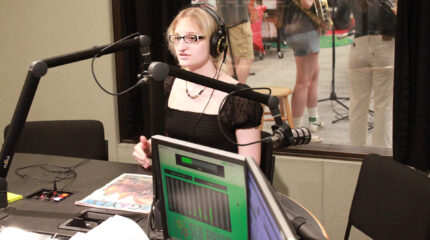 A teen wearing headphones speaking into a microphone in a radio studio