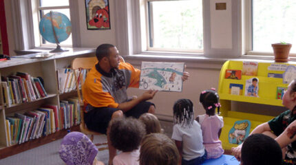 An adult showing eight youth a picture book in a classroom