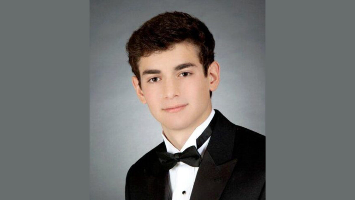 A youth wearing a tuxedo standing in front of a gradient gray background