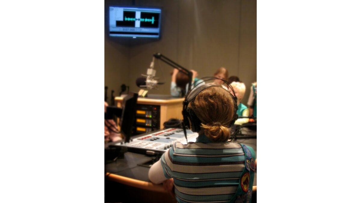A youth wearing headphones looking at an audio mixer and a microphone in a radio studio