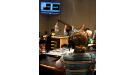 A youth wearing headphones looking at an audio mixer and a microphone in a radio studio