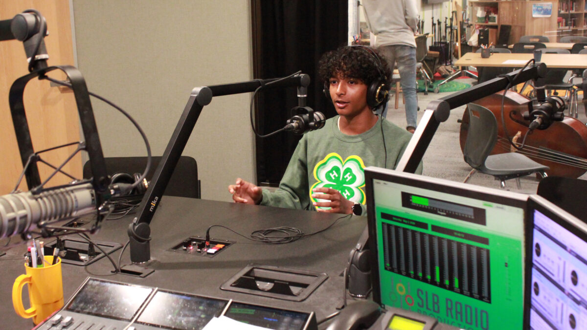 A teen wearing headphones speaking into a microphone in a radio studio
