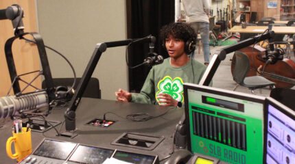 A teen wearing headphones speaking into a microphone in a radio studio