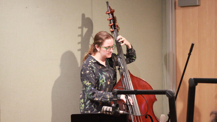 An adult playing upright bass and singing into a microphone in a radio studio