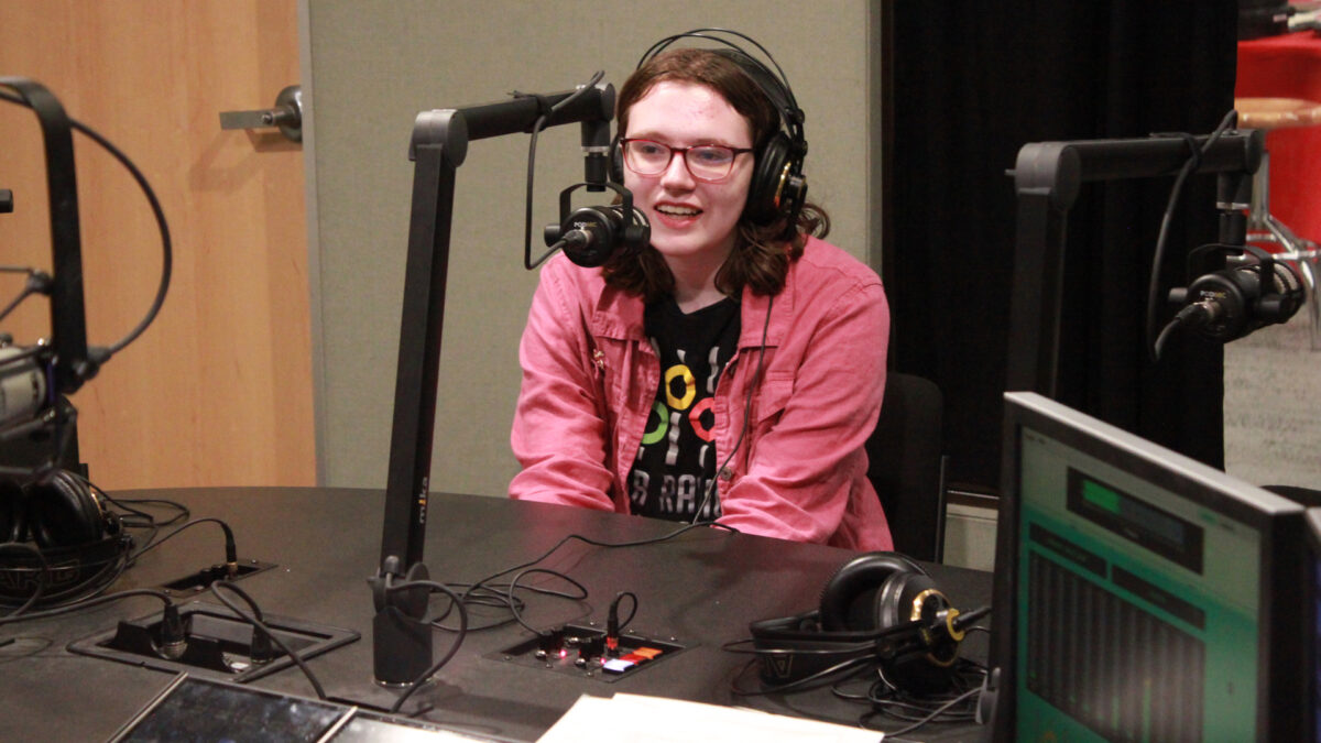 A teen wearing headphones speaking into a microphone in a radio studio
