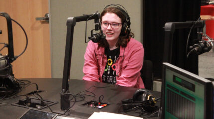 A teen wearing headphones speaking into a microphone in a radio studio
