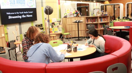 Three teens sitting around a round red couch writing on pieces of paper