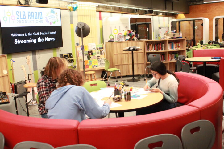 Three teens sitting around a round red couch writing on pieces of paper