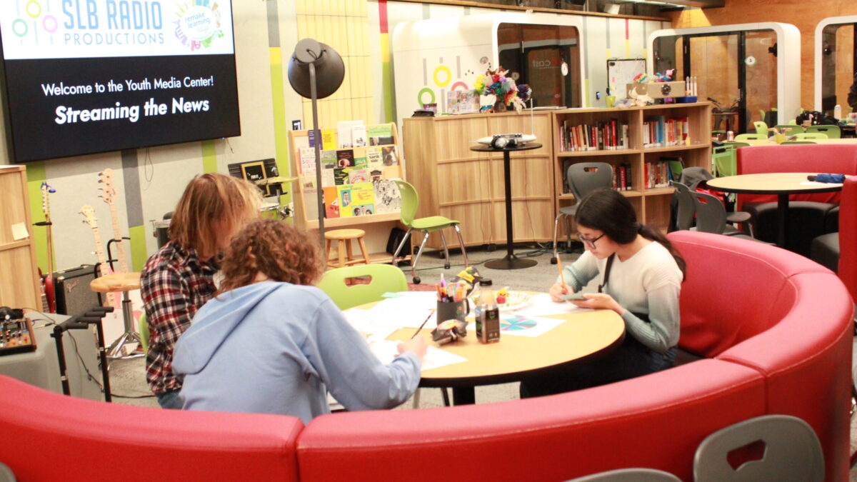 Three teens sitting around a round red couch writing on pieces of paper